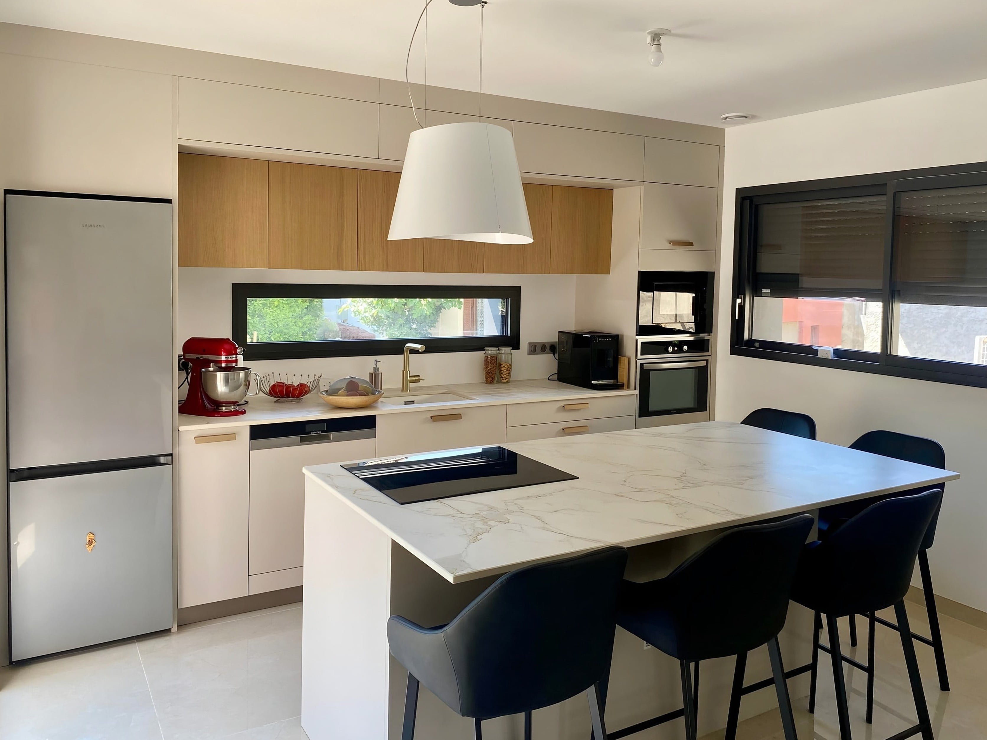 Cuisine en chêne naturel et cachemire avec îlot en céramique veinée, grande suspension blanche et chaises bleu nuit
