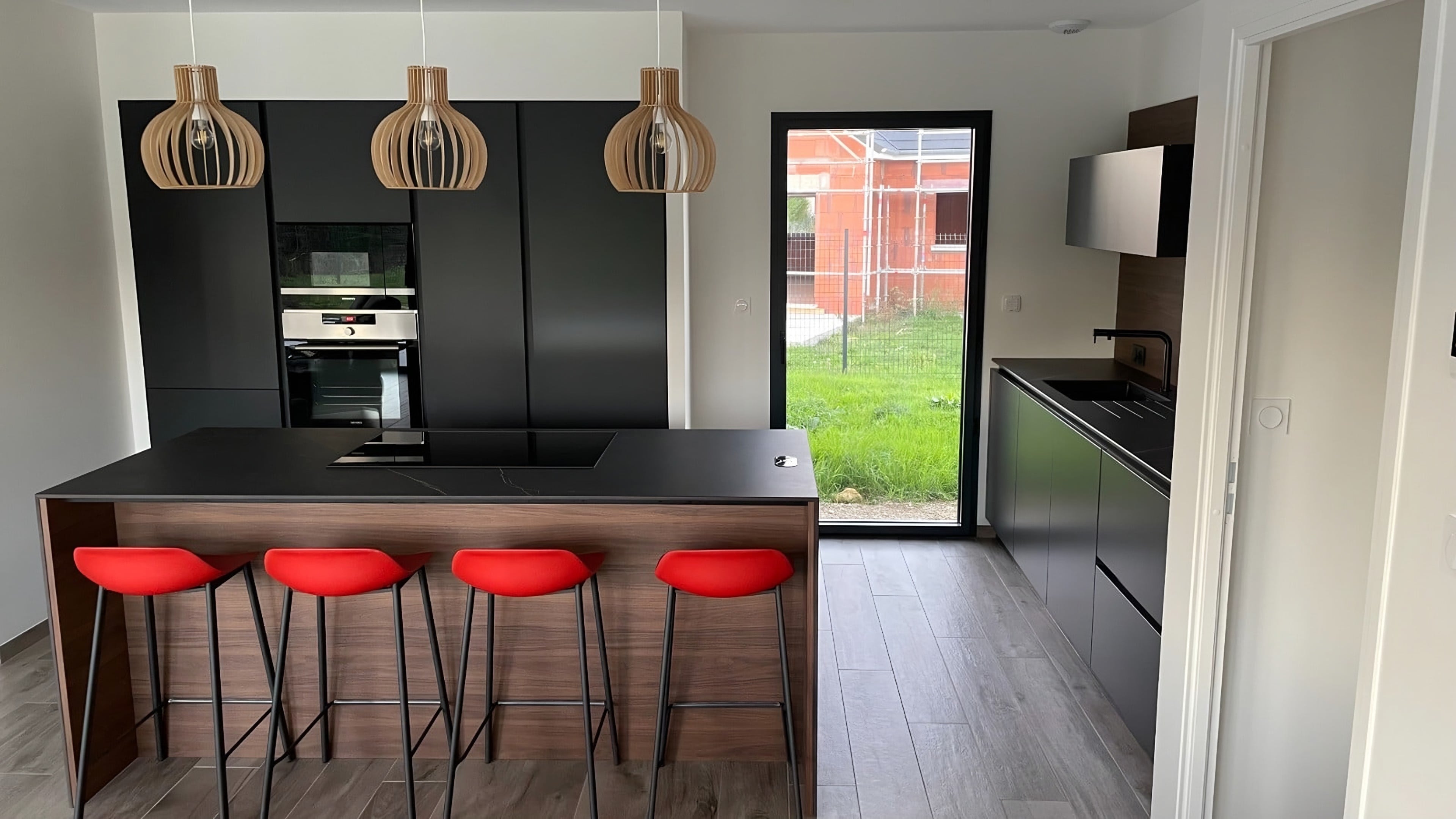 Cuisine aux colonnes laquées gris anthracite mat, îlot en noyer foncé avec tabourets rouges et suspensions en bois