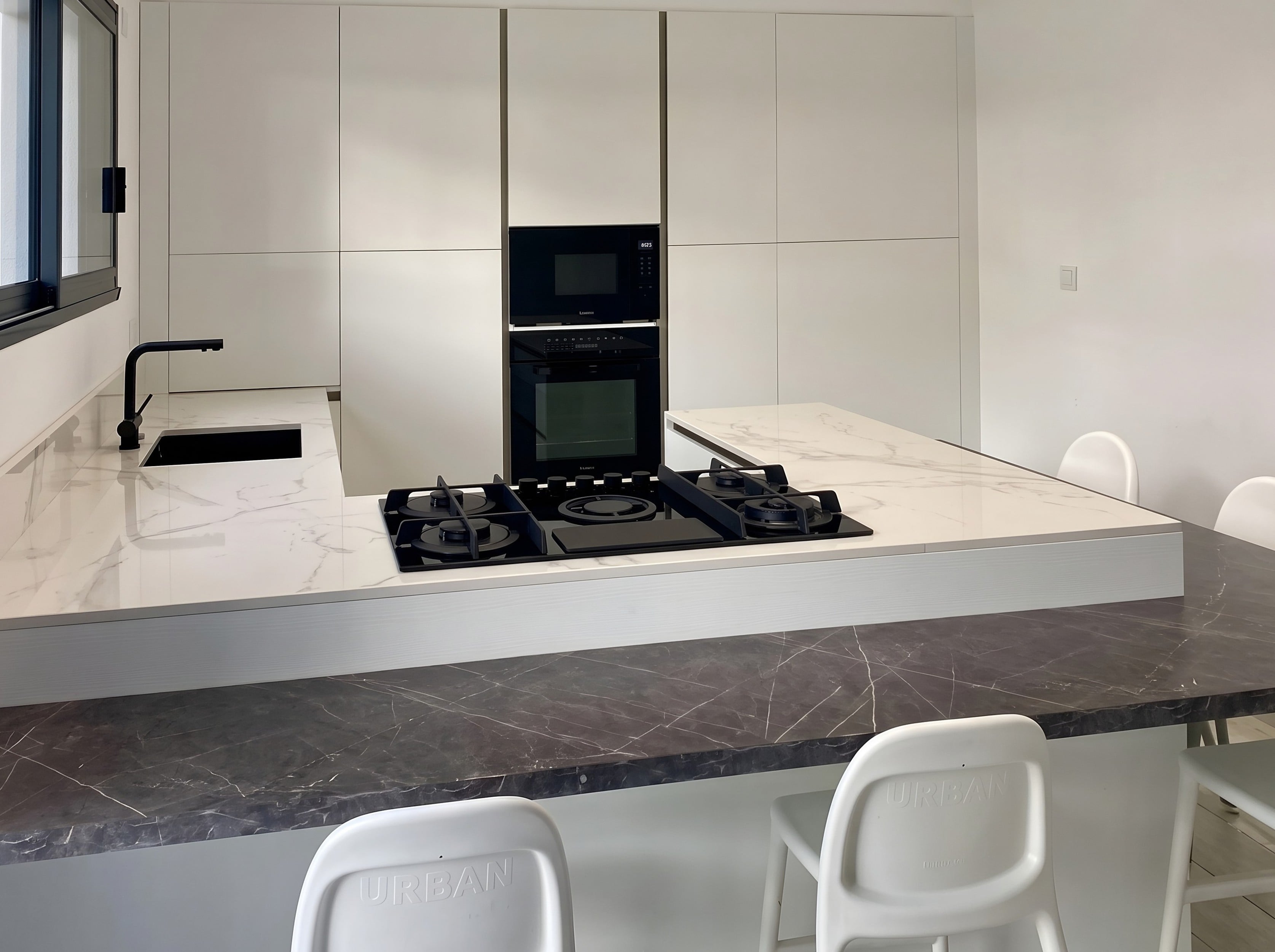 Plan de travail en quartz Calacatta Gold avec plaque de cuisson, snack en pierre sombre et chaises blanches