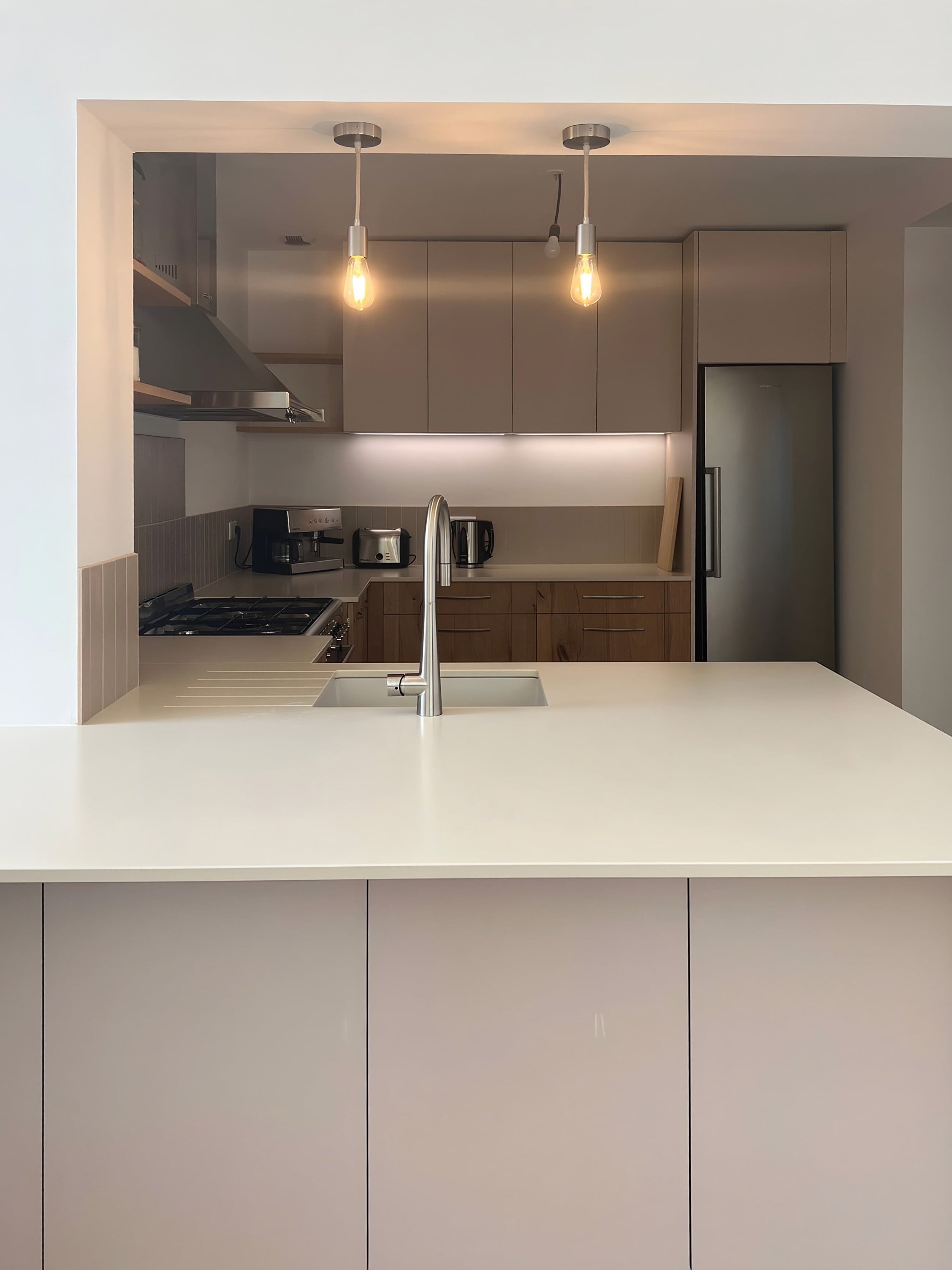 Îlot en quartz blanc et évier, meubles hauts cachemire, suspensions et réfrigérateur inox
