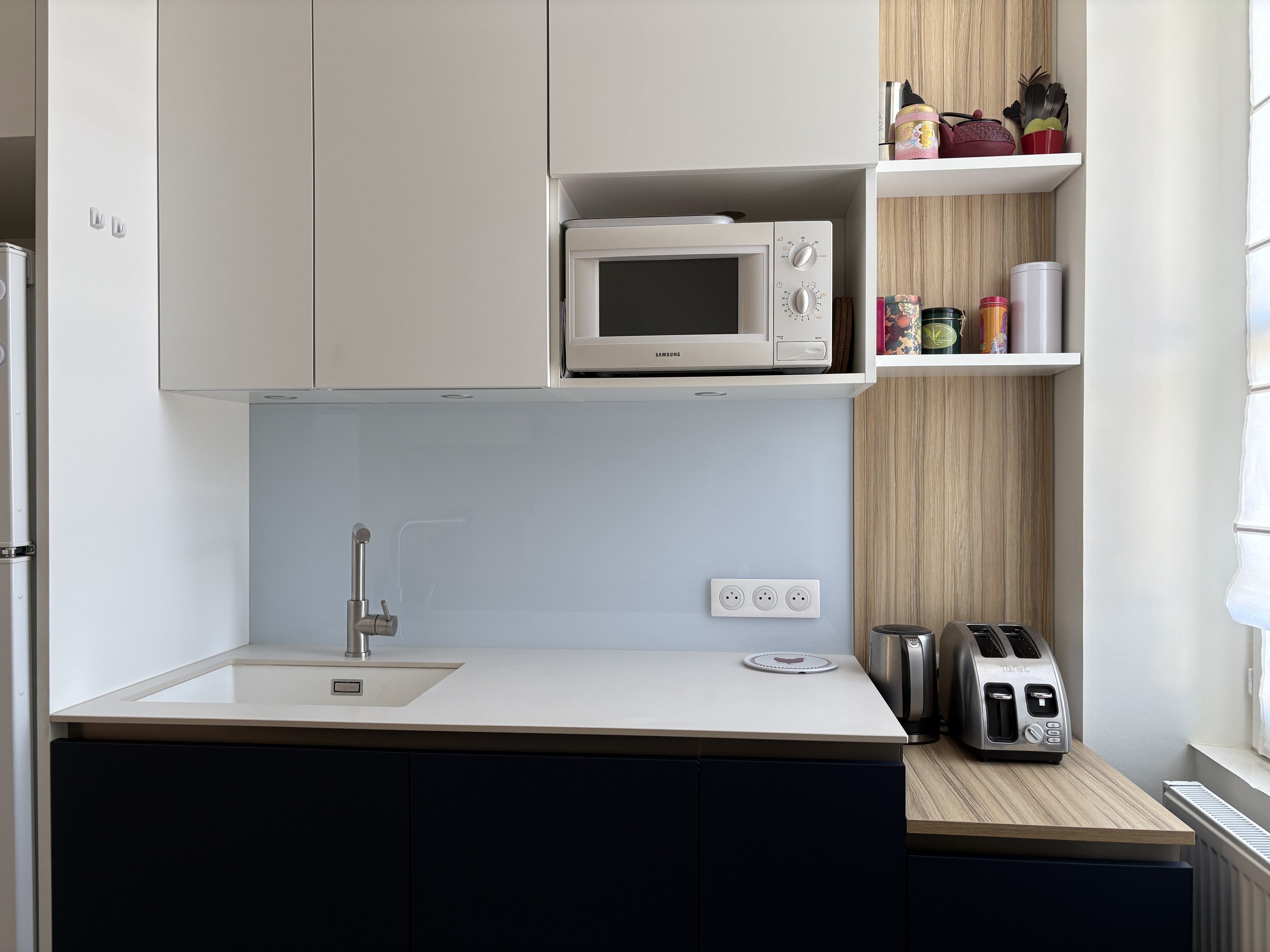Évier sous plan blanc, crédence en verre bleu pâle, meubles hauts blancs et étagères effet bois