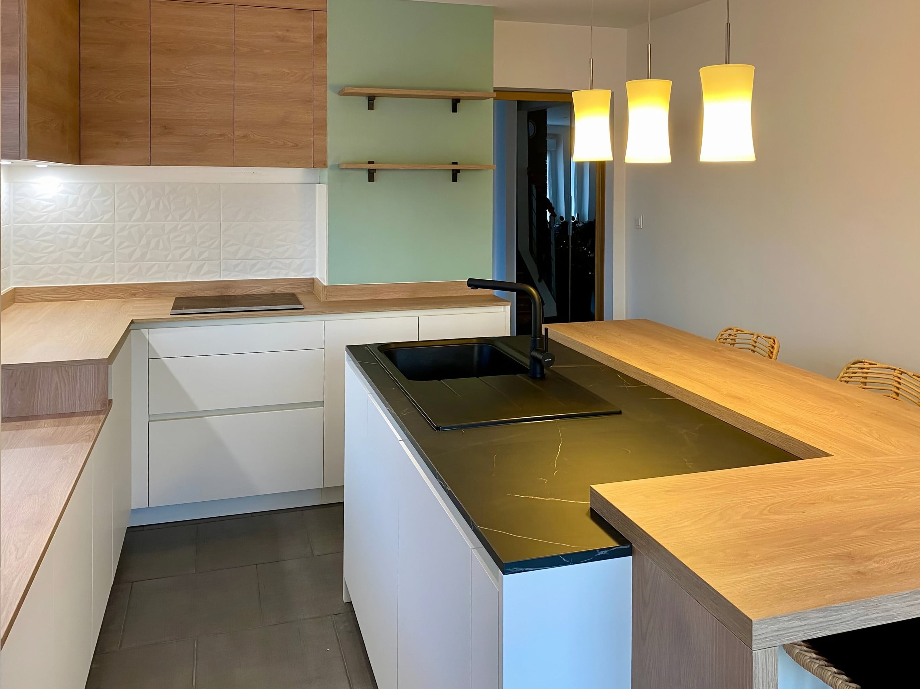 Meubles blancs sans poignées et plan stratifié effet marbre noir, étagères en chêne au-dessus de l’évier
