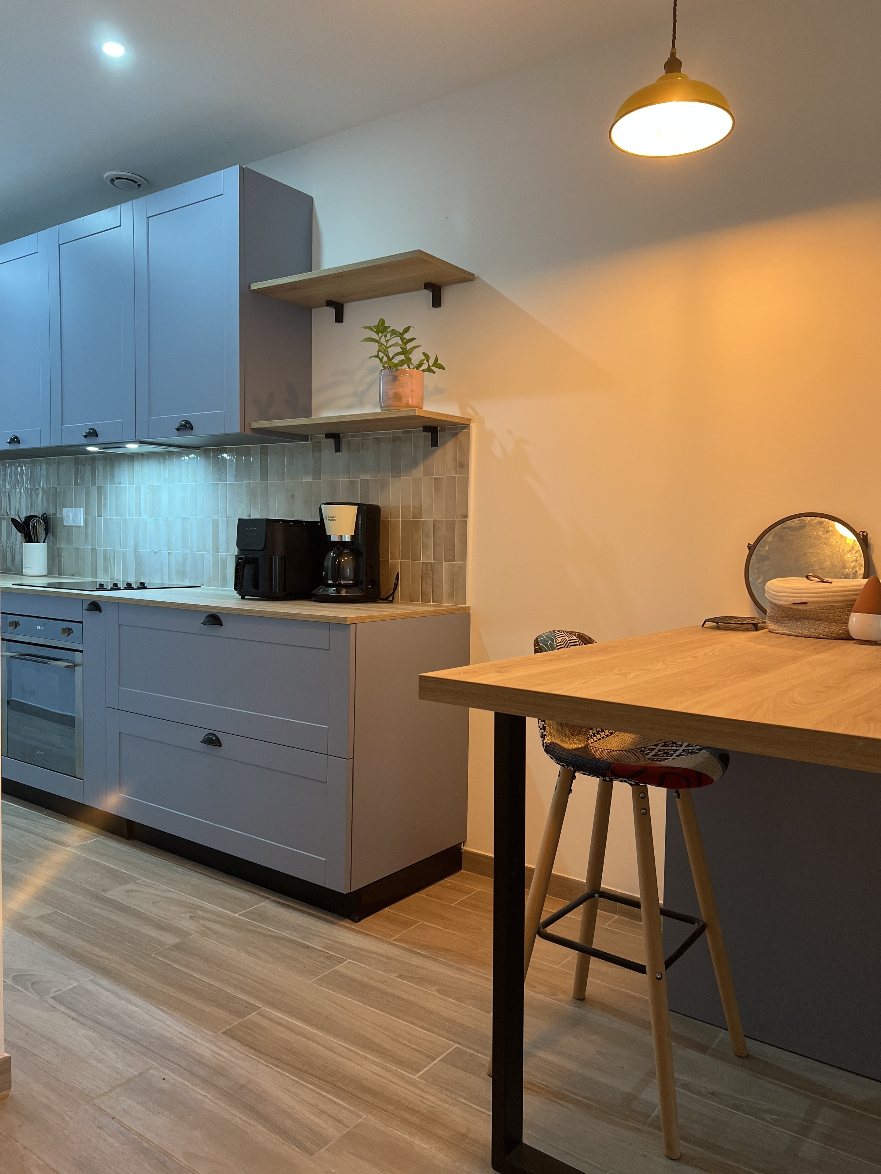 Meubles bleus à cadre et poignées coquille noires, étagères en bois, table haute effet bois sous une suspension