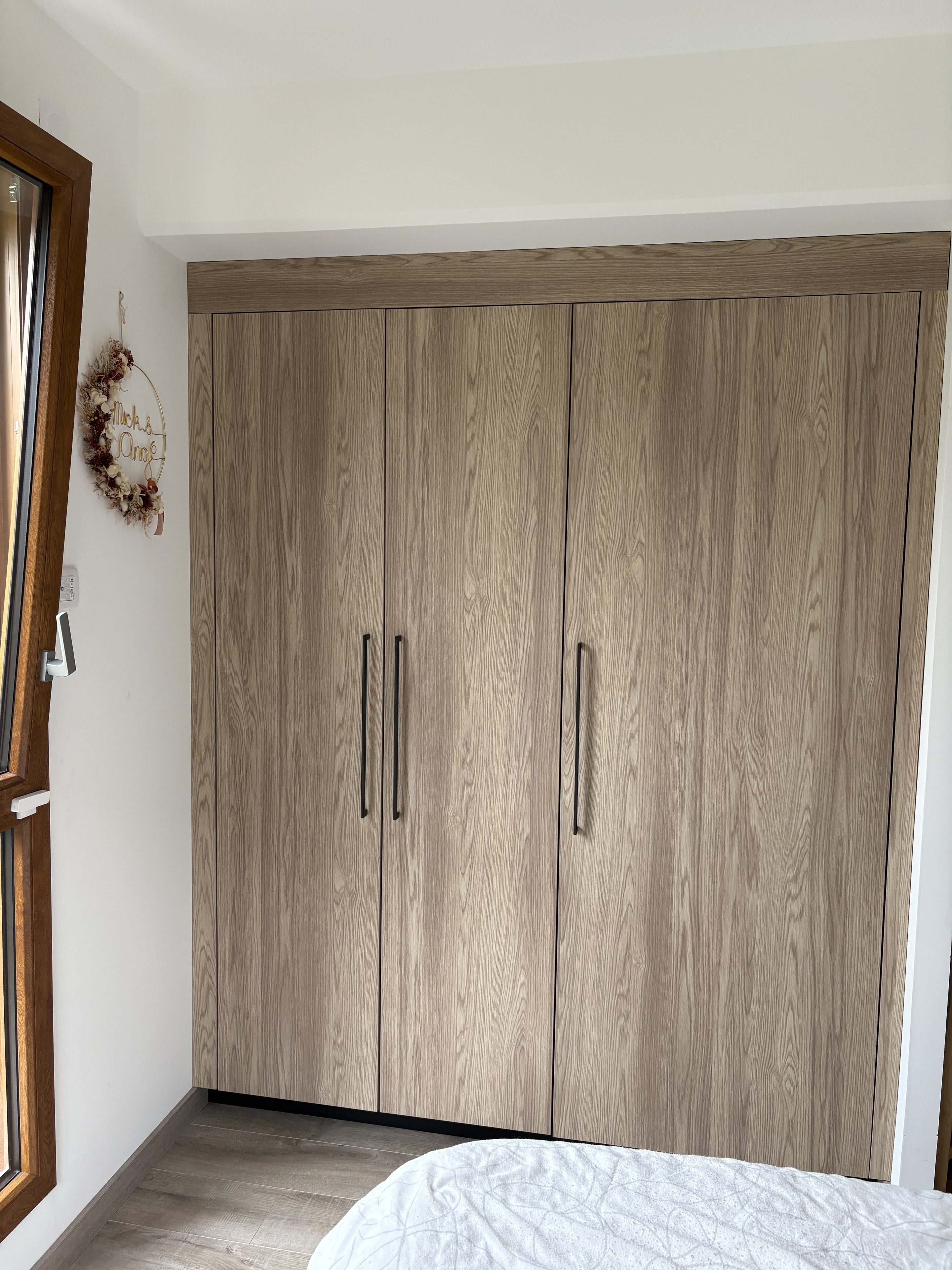 Dressing toute hauteur en décor chêne aux poignées noires, dans une chambre