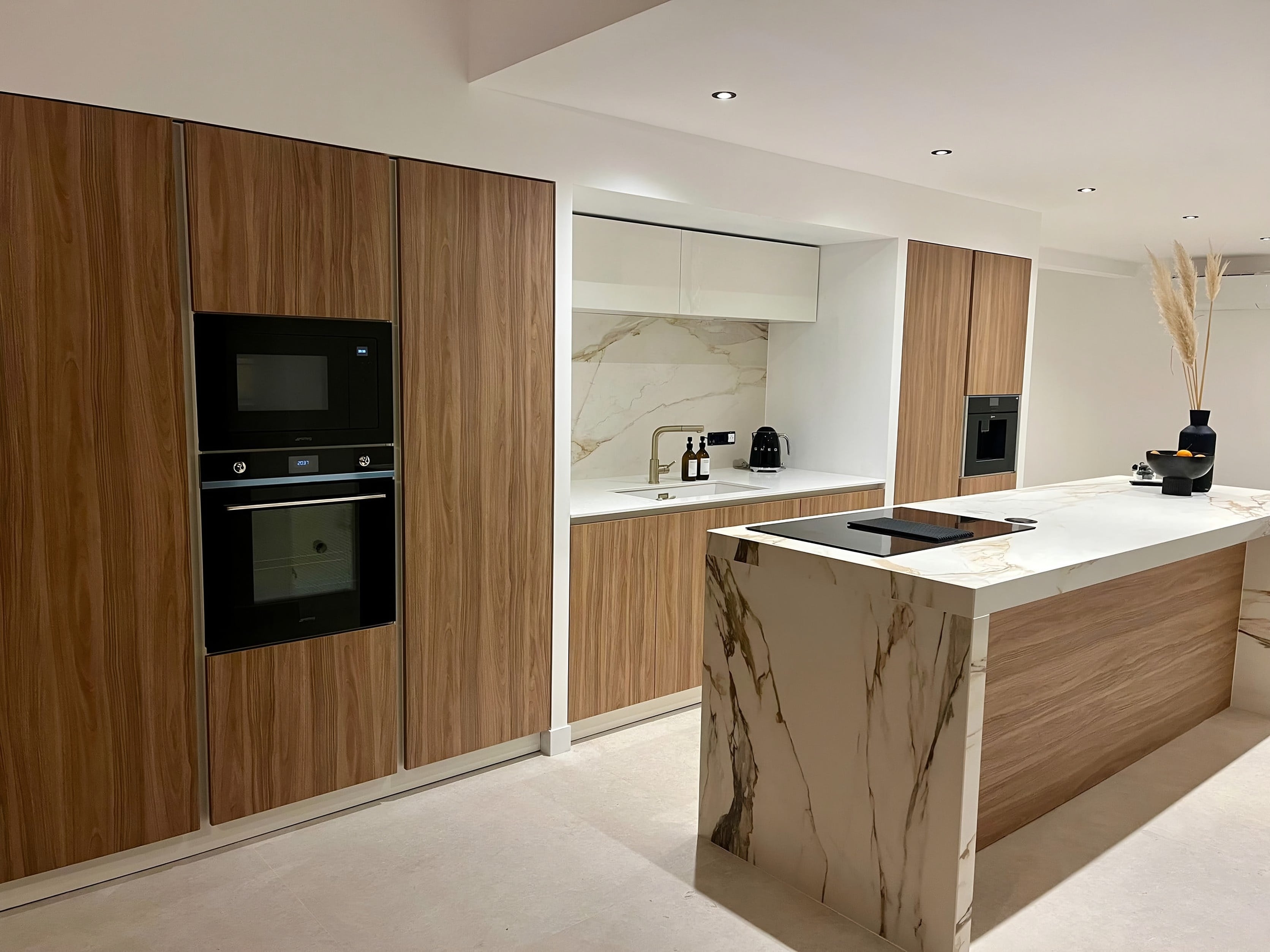 Cuisine ouverte avec colonnes en noyer caramel, fours encastrés et îlot habillé de céramique marbrée