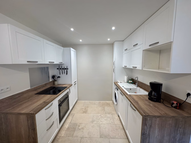 Cuisine en ligne aux meubles blancs et plan de travail effet bois, four encastré et évier sous la fenêtre